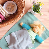 Das Puppenkind Lotti liegt unter einem Stricktuch zugedeckt, daneben ein Emaille Kännchen von Kokomoo mit frischen Blumen und ein Korb mit Tüchern und Wäscheklammern.