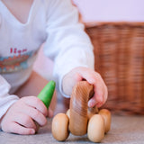 Ein Baby hält das Greifauto von Kokomoo in der linken Hand, rechts hält es eine grüne Spielfigur aus Holz.