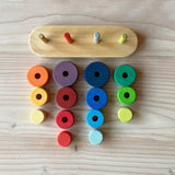 Das Grimms Steckspiel Türme "Fabuto" auseinandergebaut. Die Platte und Stäbe liegen vor den jeweils farblich sortierten Scheiben in gelb, rot, blau und grün.