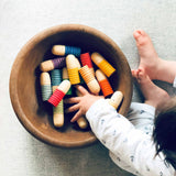 Die bunten Spielfiguren Grapat Brots liegen in einer Holzschale, ein Baby greift mit der Hand hinein.