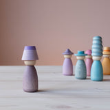 Vorne steht eine Grapat Fancy Nins Spielfigur in lila mit einem farblich passendem Hut, im Hintergrund weitere Spielfiguren aus Holz in Blau- und Lilatönen.