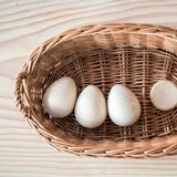Drei Holzeier und ein Holzplättchen von Grapat liegen im flachen Weidenkorb.