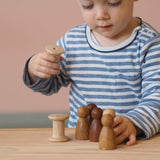 Ein Kind spielt mit den Holzfiguren Grapat "3 Nins, 3 Woods" Freunde Natur und Holzspulen.