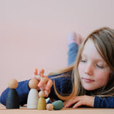 Ein Kind liegt am Bauch und spielt mit Grapat Holzfiguren, die vor ihm auf dem Boden stehen, zwei Nins in Grüntönen und die beiden Grpat Adult Nins.