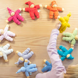 Stoffwichtel von Nanchen in elf verschiedenen bunten Farben liegen im Kreis, ein Kind schnappt sich die gelbe kleine Kuschelpuppe.