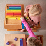 Zwei Kinder sitzen an zwei kleinen Tischen und spielen gemeinsam mit den  Holzbausteinen von Glückskäfer.