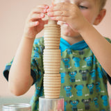 Ein Kind baut einen Turm: ganz unten eine Blechdose, dann drei Grapat "Beehive Cups" gerillte Holzbecher und darauf ein kleiner Holzpilz.