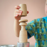 Ein Kind baut einen Turm: ganz unten eine Blechdose, dann ein Grapat "Beehive Cups" gerillter Holzbecher, darauf ein kleiner Holzpilz und ein Holzplättchen. Ein weiterer Holzbecher wird gerade oben drauf gegeben.