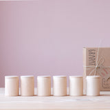 Sechs glatte Holzbecher Cups von Grapat,  mit Deckel, stehen in einer Reihe.