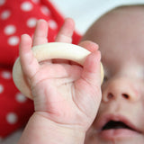 Eine Baby hält einen Holzring in der Hand und sieht ihn fasziniert an.