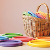 Die sechs Grapat Holzteller "Rainbow Dishes" in Regenbogenfarben nebeneinander, jeweils mit einem farblich passenden Motorikring darauf.
