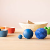 Ein blauer Kokomoo Häkelball, eine Grapat Holzkugel und eine Grapat Murmel aus Holz nebeneinander.