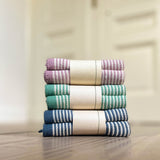 Die gestreiften kleinen Stricktücher in den Farben rosa-weiß, grün-weiß und blau-weiß zusammengefaltet auf einem Stapel.