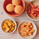Ein oranges Jutekörbchen mit orangen Kokomoo Häkelbällen, drei Holzschalen mit kegelförmigen, orangen Grapat Mandalasteinen, nach Orangeton sortiert.