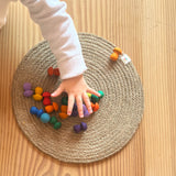 Eine Kinderhand greift nach den Mandala Pilzen von Grapat "Mushrooms Rainbow", die auf einem runden Tischset liegen.
