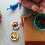 Körbe und Schalen mit Grapat Mandala Regenbogen Eier, ein Kind, auf einem Pikler Podest sitzend, spielt gerade damit.