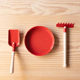 Sandschaufel, Metallsieb und Mini-Metallrechen in rot von Glückskäfer für Kinder zum Spielen bereit gelegt.