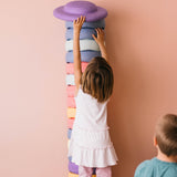 Ein Kind möchte ein Stapelstein® Balanceboard in violett ganz oben auf einen riesigen, es überragenden Stapelstein Turm legen.