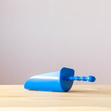 Eine kleine blaue Sandschaufel für Kinder liegt auf einem Holzboden.