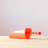 Eine kleine rote Sandschaufel für Kinder liegt auf einem Holzboden.