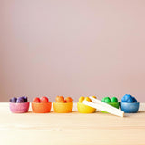 Grapat "Bowls and Acorns" Sortierspiel: das sind kleine Holzeicheln in Regenbogenfarben und 6 bunte Holzschälchen ebenfalls in Regenbogenfarben - hier sortiert aufgestellt, die kleine Holzzange ist auch dabei.