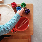 Ein Kind sortiert die bunten kleinen Holzeicheln in Regenbogenfarben vom Sortierspiel Grapat "Acorns & Bowls" farblich passend in die Holzschälchen.