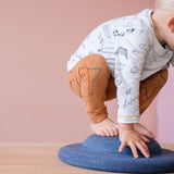 Ein Kleinkind balanciert auf dem Stapelstein® Balance Board in blau, das flach auf dem Boden liegt, mit dem Knubbel nach oben.