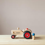 Der Fagus Traktor aus Holz von der Seite, eine Spielfigur sitzt im Traktor, eine steht daneben.
