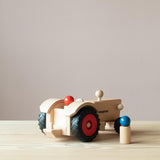 Der Fagus Traktor aus Holz von schräg hinten, sodass die Anhängerkupplung zu sehen ist, eine Spielfigur sitzt im Traktor, eine steht daneben.