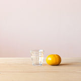 Ein Pikler Trinkglas für Kinder mit 13cl, daneben liegt eine Mandarine, sodass man einen guten Größenvergleich hat.