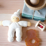 Ein weißer Wichtel aus weichem Stoff, ein Panda Beißring, eine kleine Babyrassel, gestrickte Baumwolltücher in Blautönen und ein Jutekorb mit Holzkugel darin. Perfekt für ein Babygeschenk.