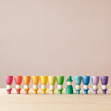 Die 12 "Wizards" Zauberer Spielfiguren aus Holz von Grapat stehen sortiert nach den Regenbogenfarben in einer Reihe, alle auf dem Kopf, bis auf dunkelgrün, der fünfte von rechts.